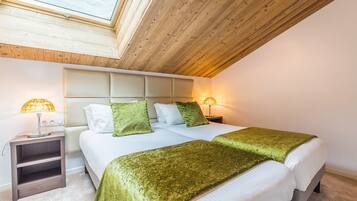 A bedroom with a skylight, two beds with green bedding, a nightstand with a lamp, and a wooden ceiling.