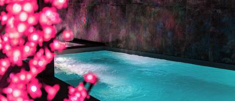 A modern spa area with a large bathtub and a wall-mounted screen displaying a nature scene.