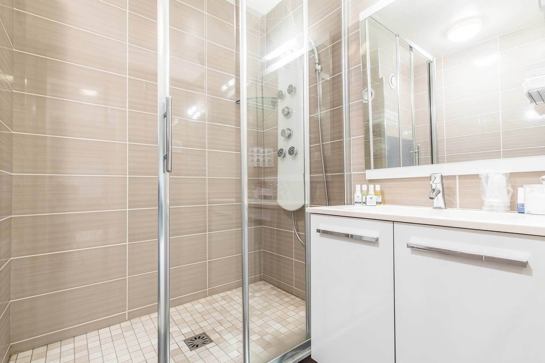 A modern bathroom with a glass-enclosed shower, white tiled walls, and a large mirror above the sink.