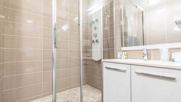 A modern bathroom with a glass-enclosed shower, white tiled walls, and a large mirror above the sink.