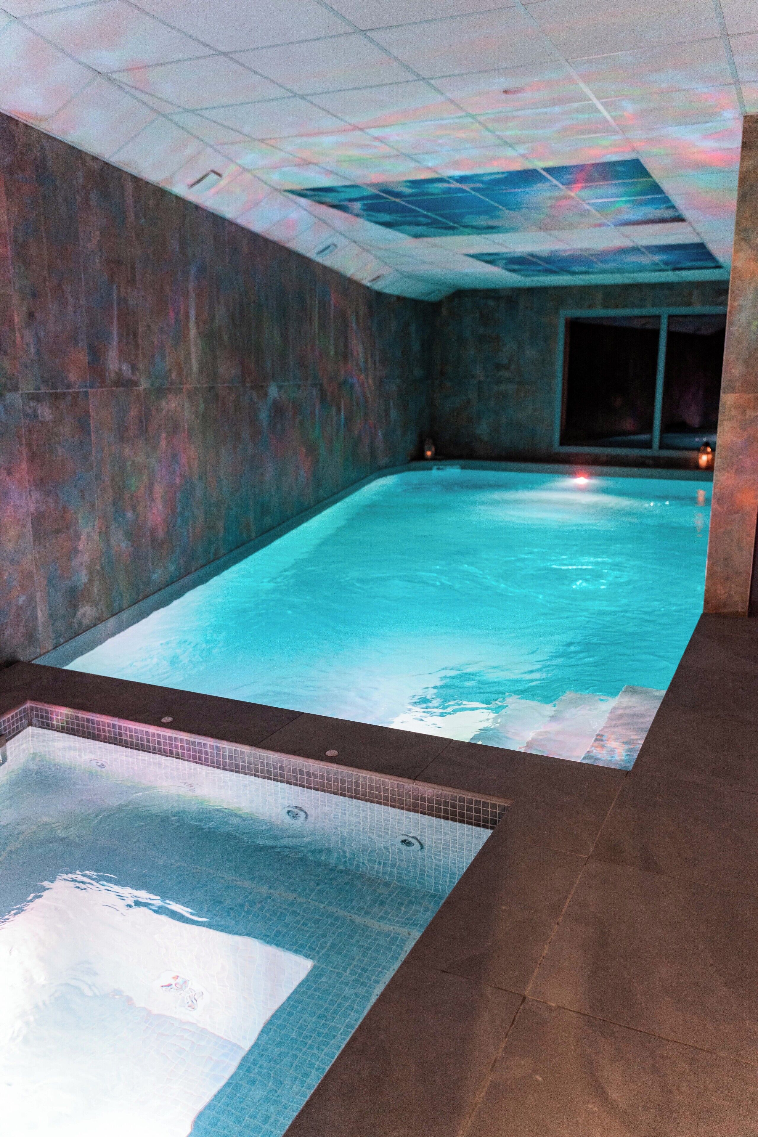 A swimming pool with a ceiling projection, tiled walls, and a separate hot tub area.