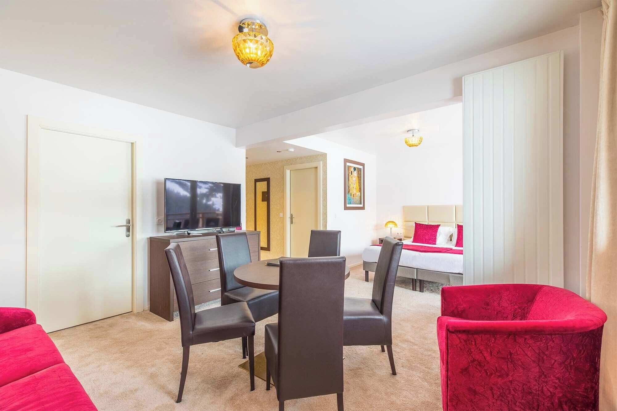 A hotel room with a dining area, a TV, a bed, and a red chair.