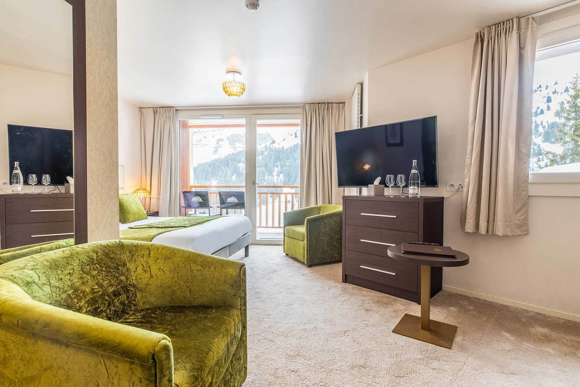 Habitación de hotel con cama, televisión, escritorio y balcón con vista a la montaña.
