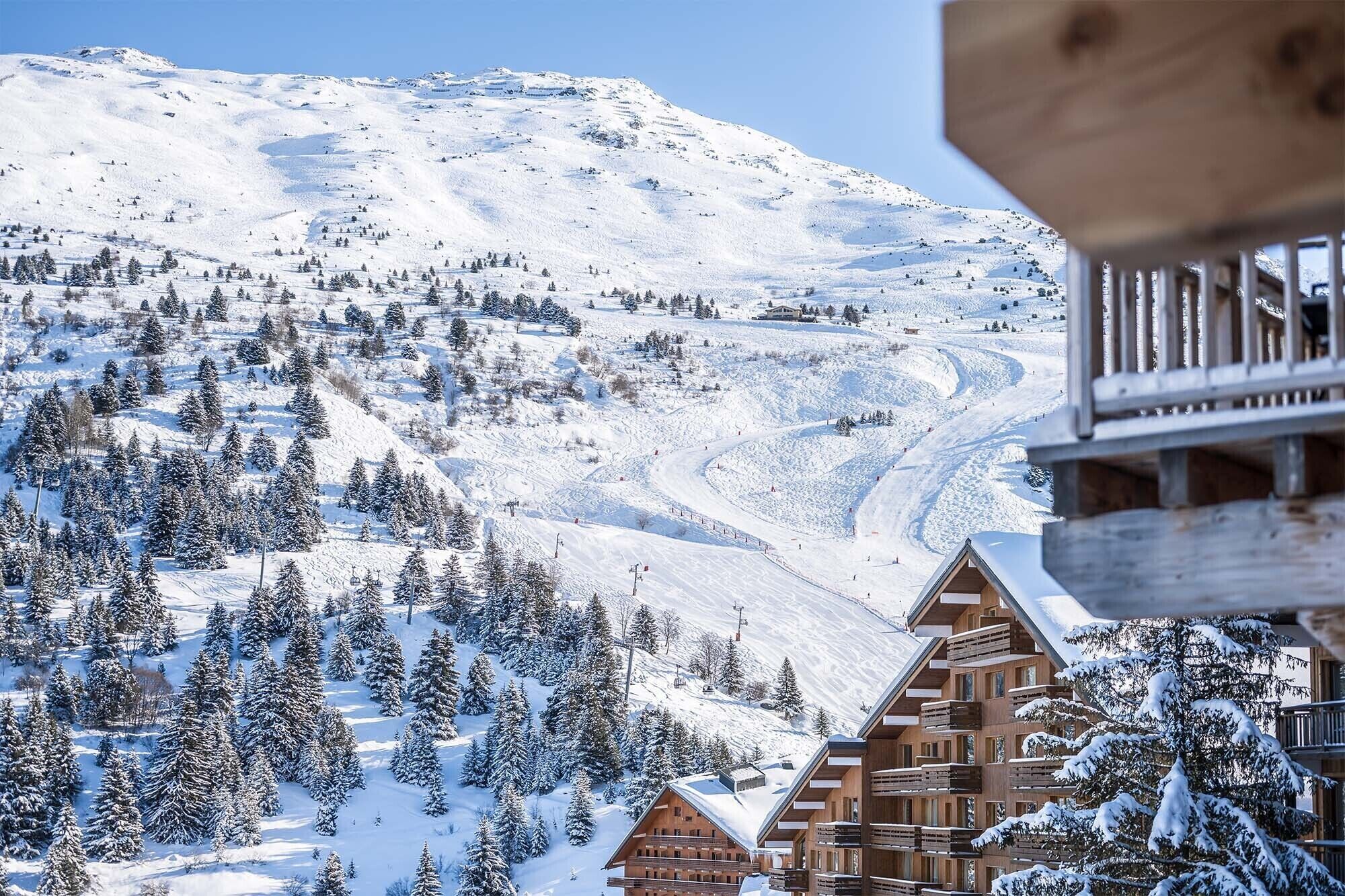 Een besneeuwd berglandschap met een wintersportgebied, houten chalets en een skilift.
