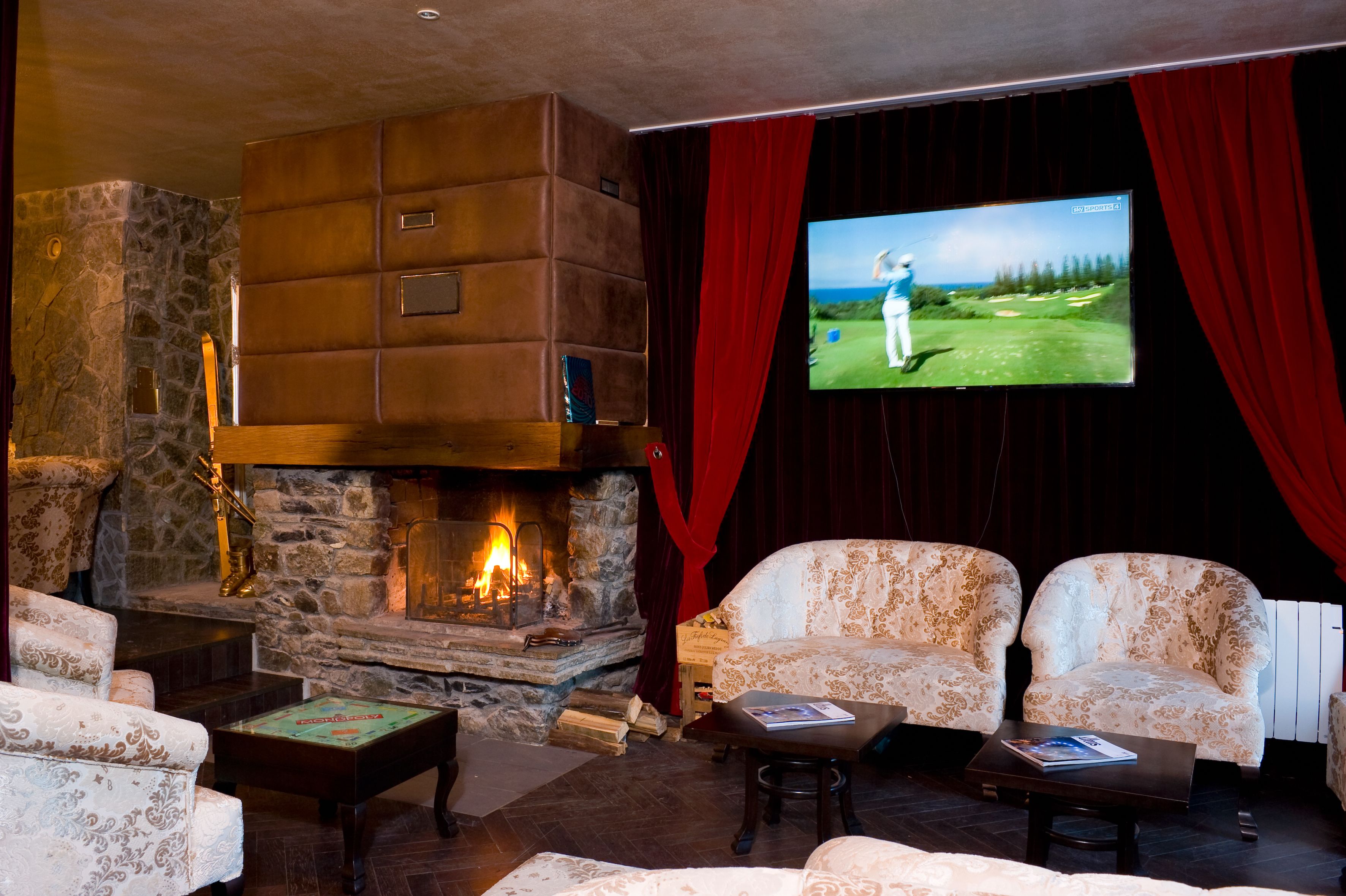 A cozy room with a stone fireplace, comfortable seating, and a large screen displaying a golf game.