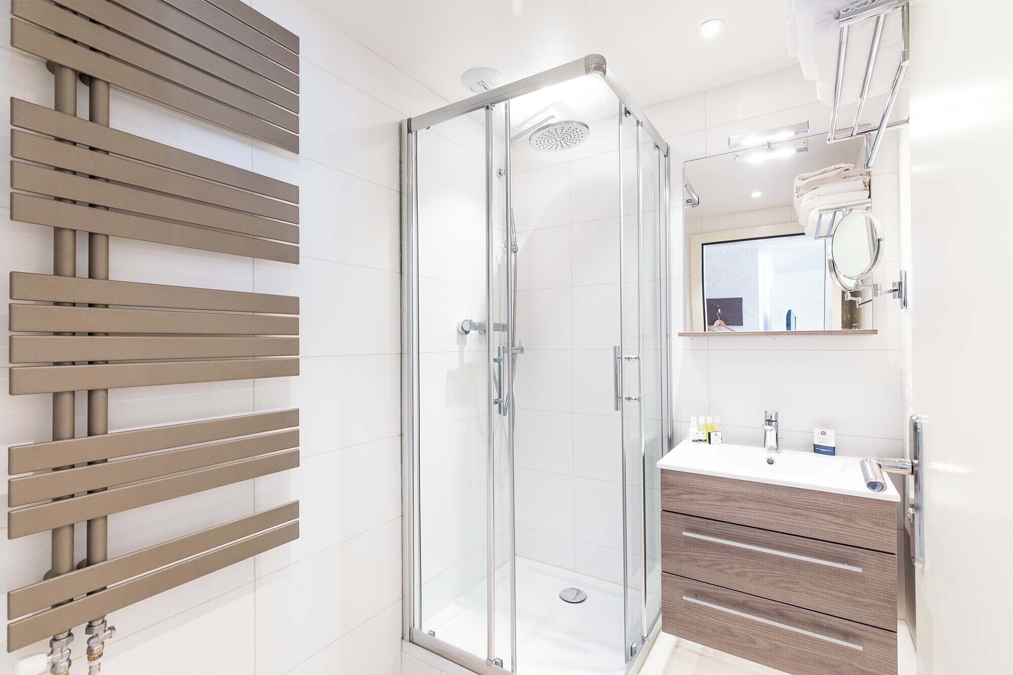 A modern bathroom with a glass-enclosed shower, a wooden panel wall, a vanity with a mirror, and a towel rack.
