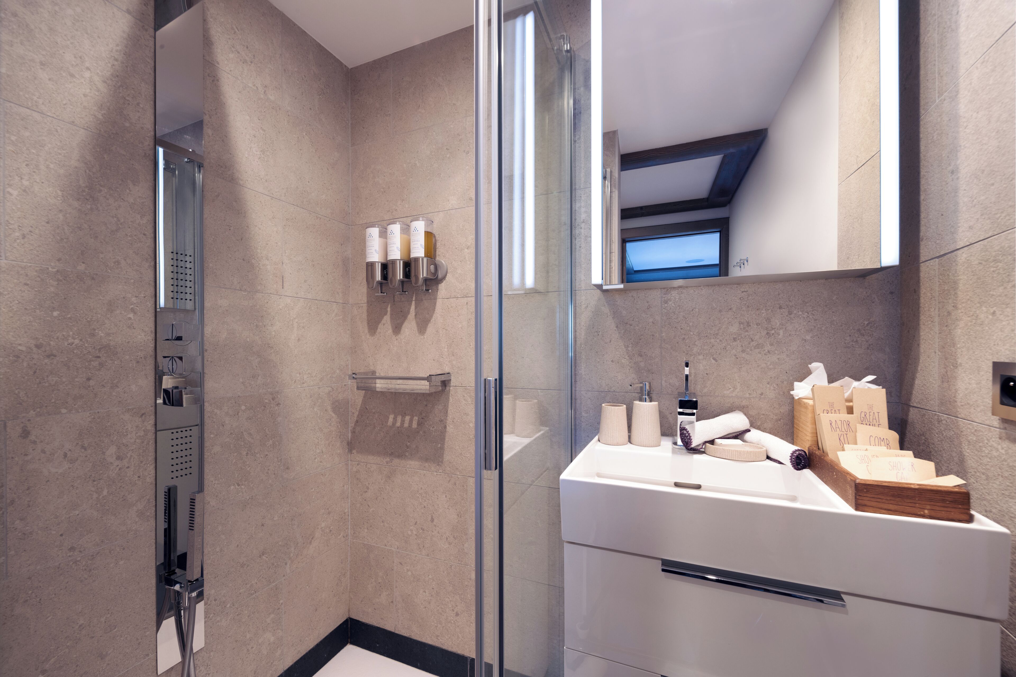 A modern bathroom with a glass shower enclosure, a white sink with toiletries, and a large mirror.