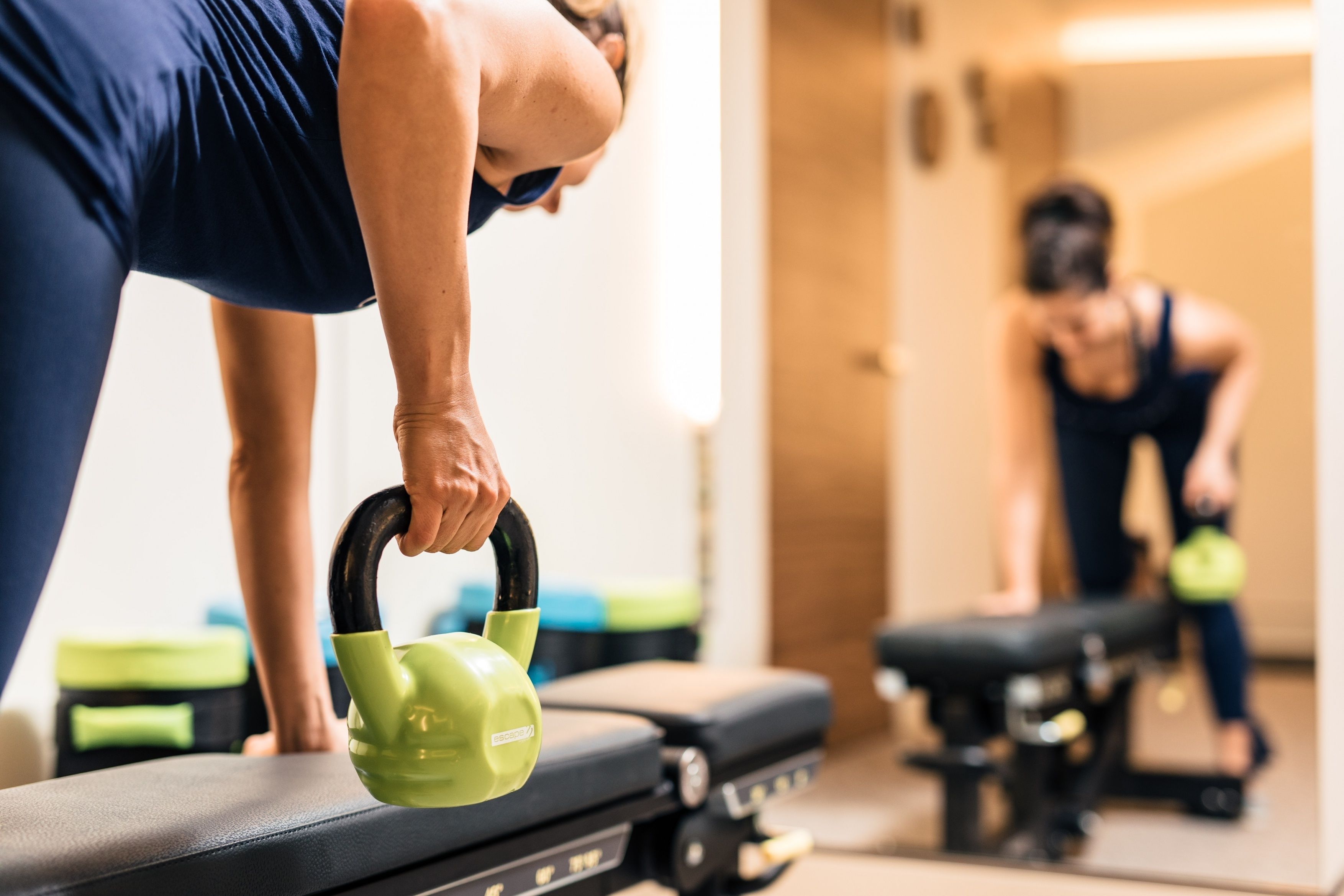 A person performing a kettlebell exercise in a gym with exercise equipment and a mirror.