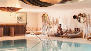 A modern indoor pool area with lounge chairs, a wooden bench, and a unique ceiling design. - Six Senses Residences Courchevel (Courchevel)