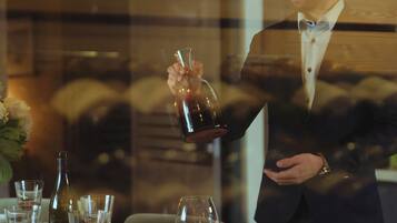 Una persona sirve una bebida en un vaso sobre una mesa con otros vasos y una botella.
