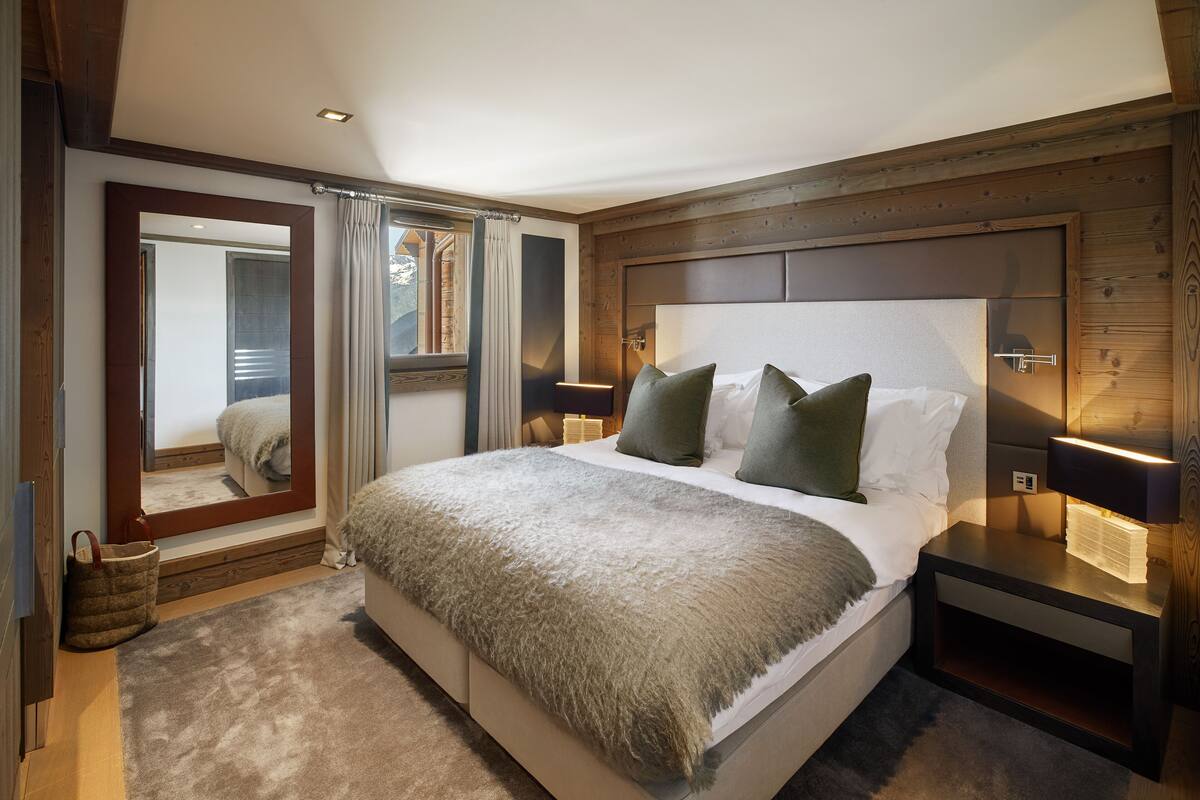 Een moderne slaapkamer met een groot bed, een houten hoofdbord, nachtlampjes en een spiegel.
