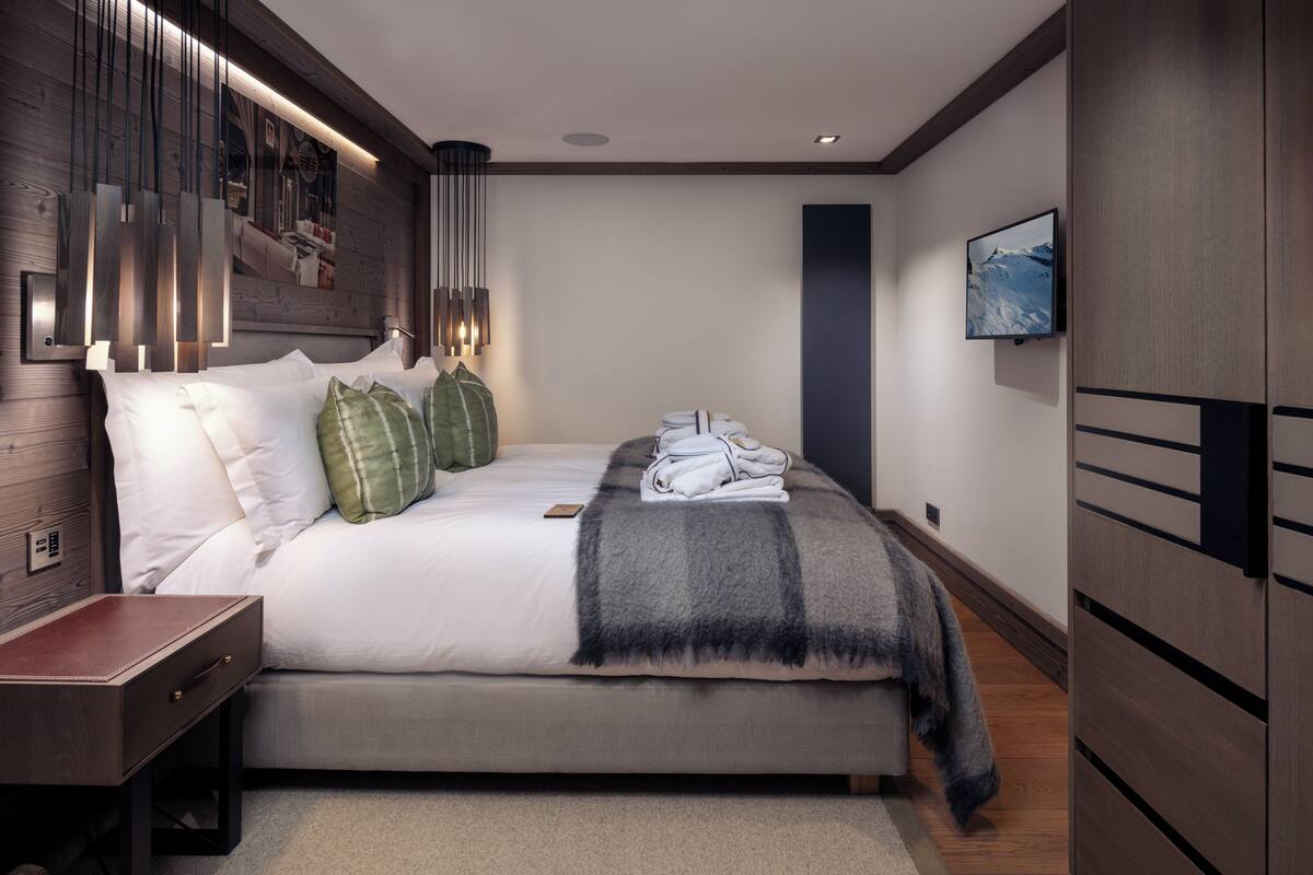 Een moderne slaapkamer met een groot bed, een nachtkastje, een aan de muur bevestigde televisie en een houten hoofdbord.