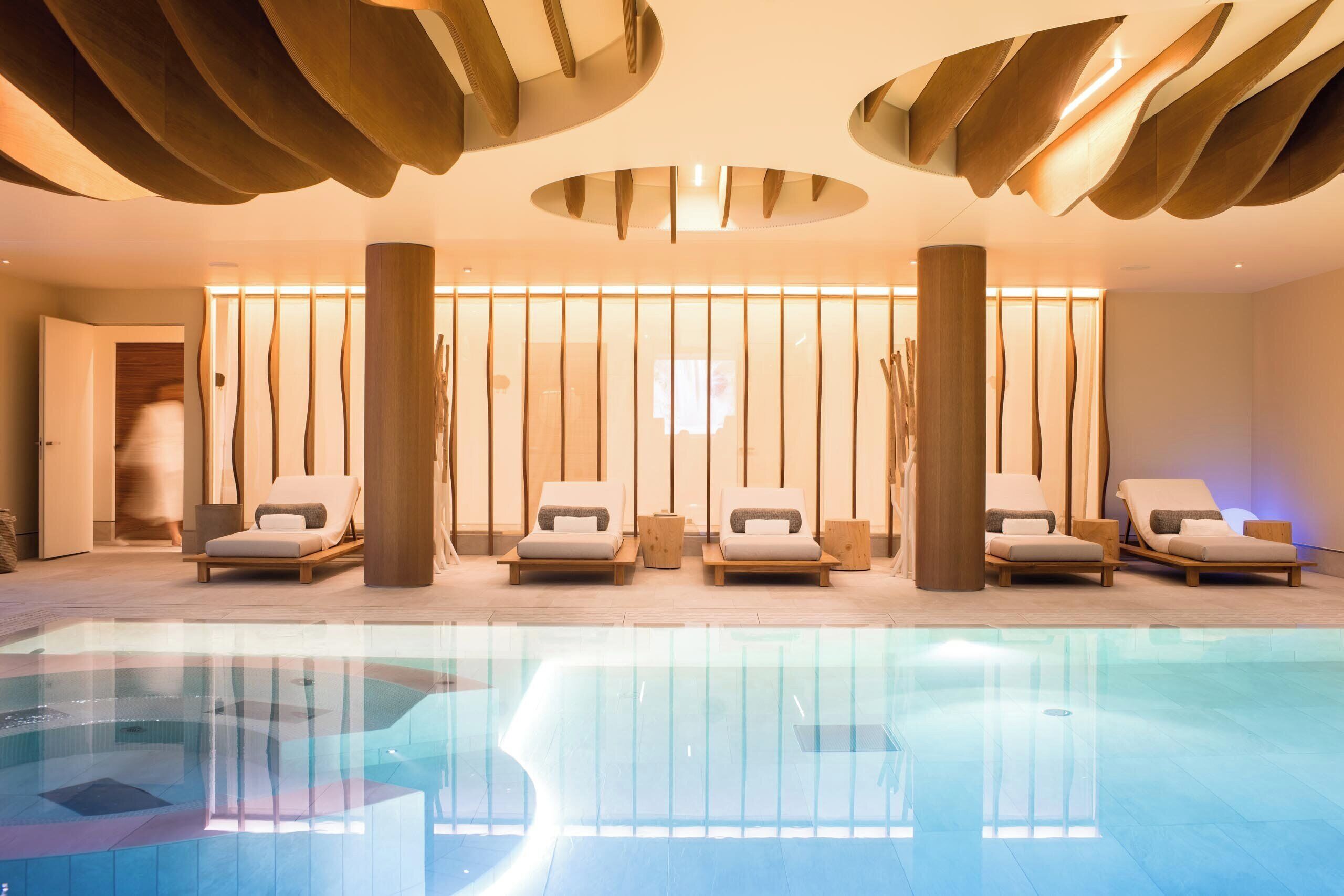 A modern spa with a glass pool, wooden loungers, and a minimalist design.