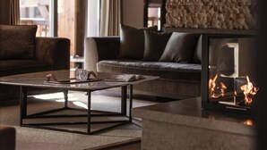 A cozy living room with a stone wall, a fireplace, and a modern chandelier. - Six Senses Residences Courchevel (Courchevel)