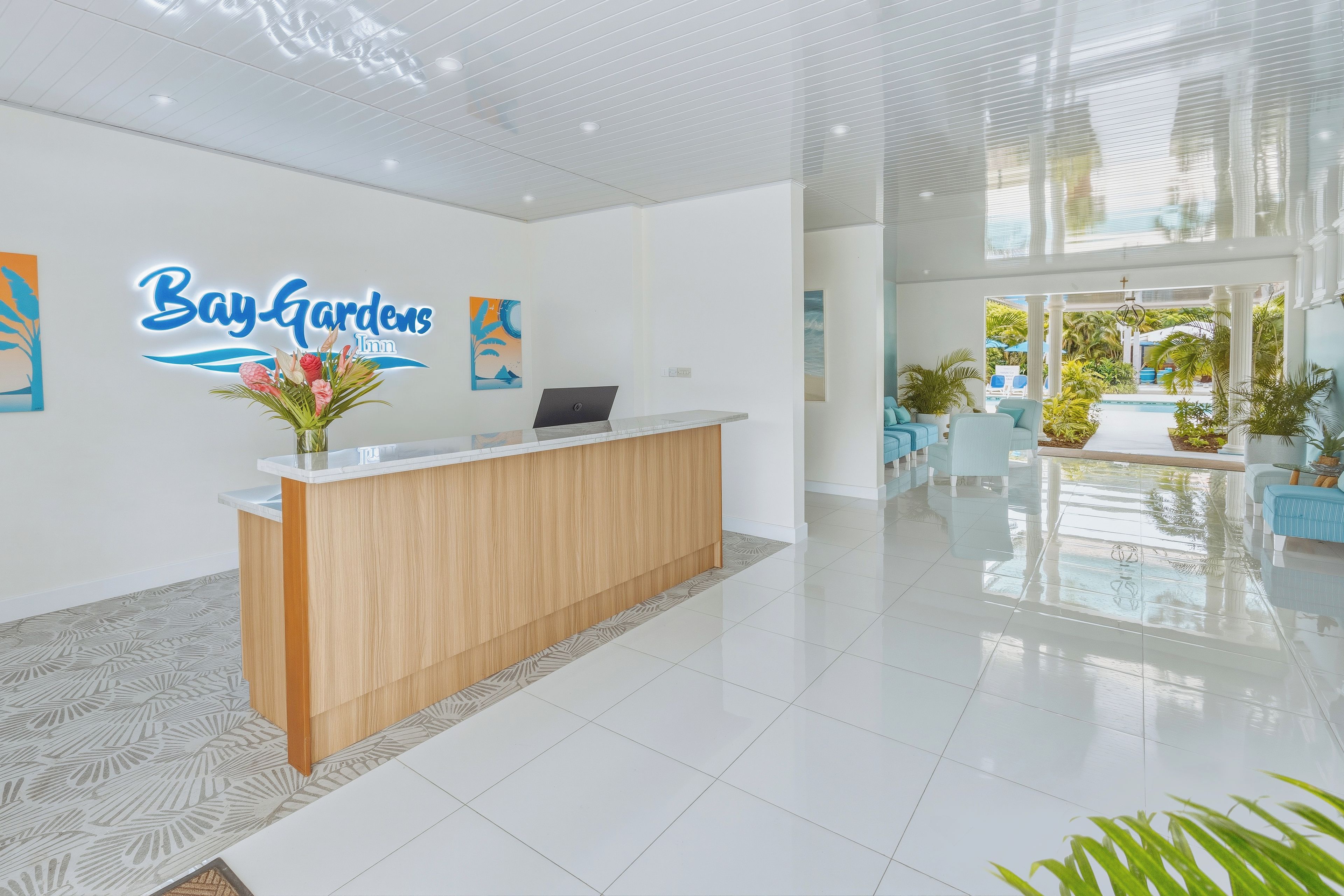 A hotel reception area with a wooden reception desk, a laptop, and a wall sign that reads 'Bay Gardens Inn'.