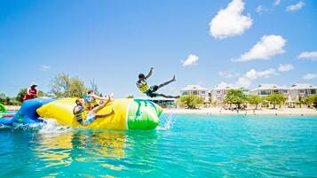 A water park with inflatable water slides and a beach area with buildings in the background.