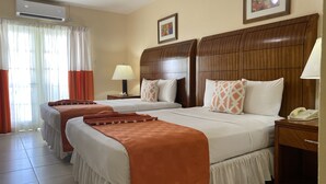 A hotel room with two beds, a wooden headboard, a nightstand with a phone, and a window with curtains. - Bay Gardens Inn (Gros Islet)