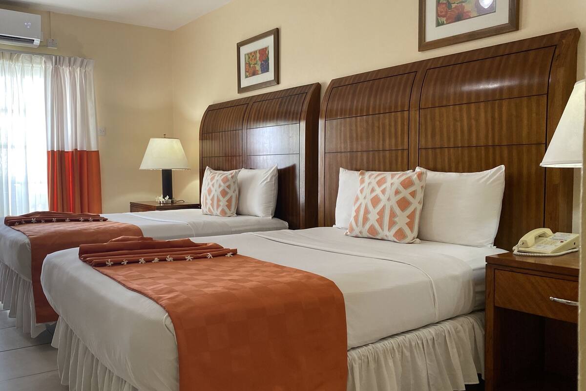 A hotel room with two beds, a wooden headboard, a nightstand with a phone, and a window with curtains.