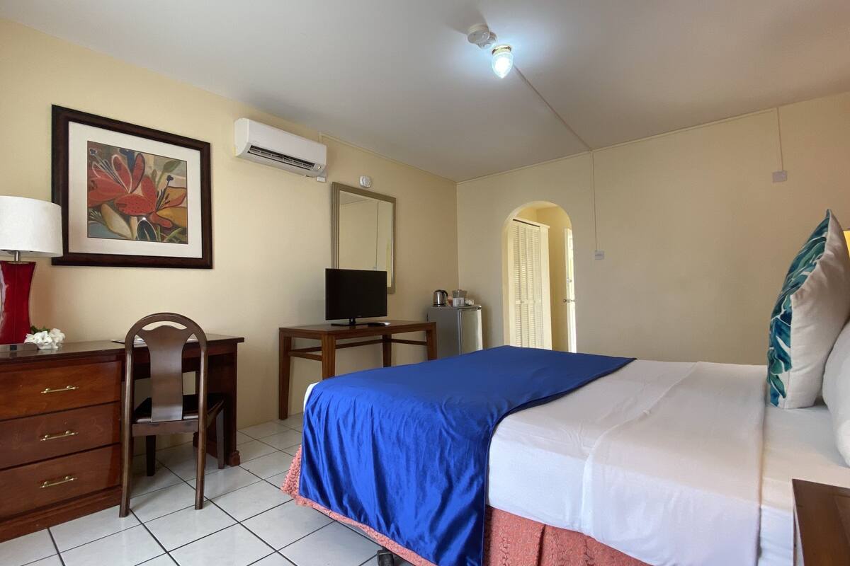 A hotel room with a bed, desk, chair, dresser, and an air conditioning unit.