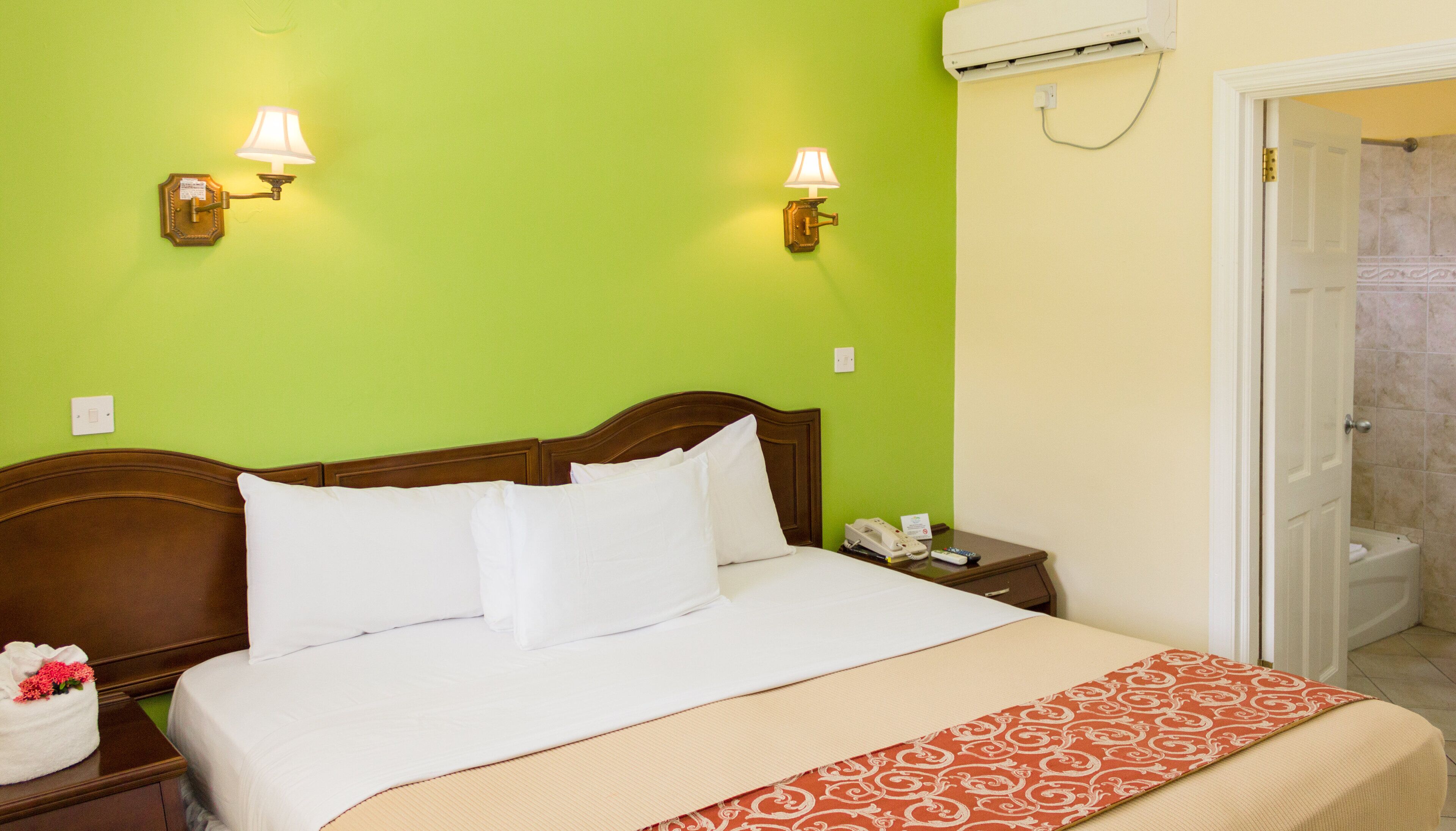Une chambre d’hôtel avec un lit, des tables de chevet, une commode, une lampe, un téléphone et une porte de salle de bain.