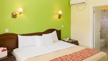 Une chambre d’hôtel avec un lit, des tables de chevet, une commode, une lampe, un téléphone et une porte de salle de bain.