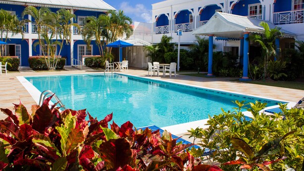 A pool area with a clear blue pool, white lounge chairs, and a building with blue and white architecture. - Bay Gardens Inn (Gros Islet)