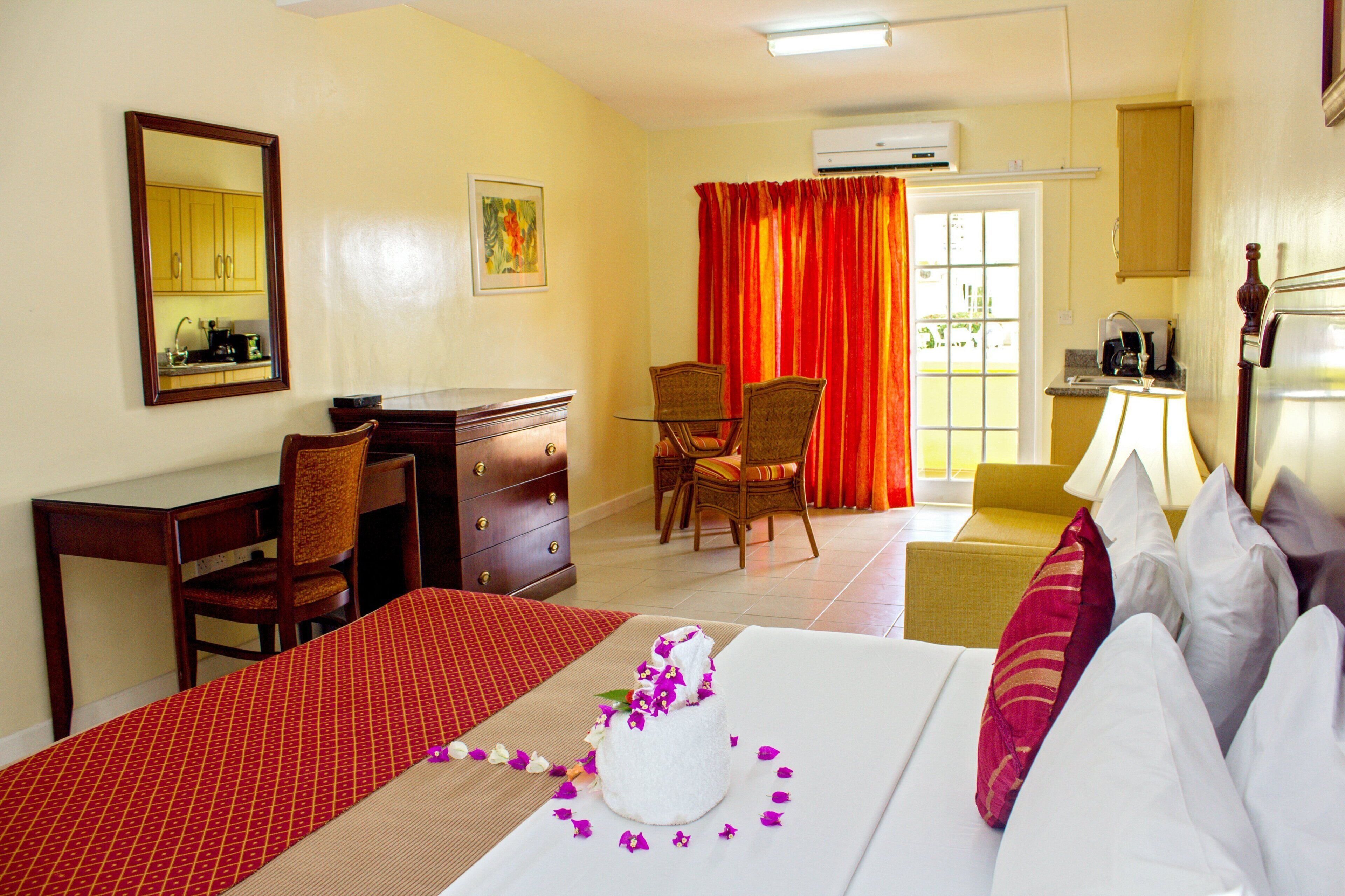 A hotel room with a bed, a desk, a chair, a dining area, and a kitchenette.