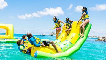 People on inflatable water slides in a clear blue water setting.