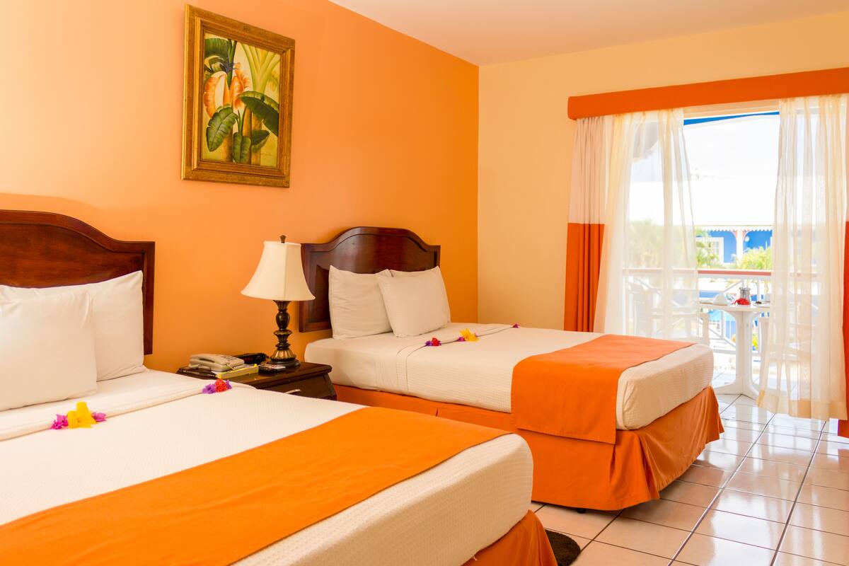 A hotel room with two beds, a painting on the wall, and a balcony with a view.