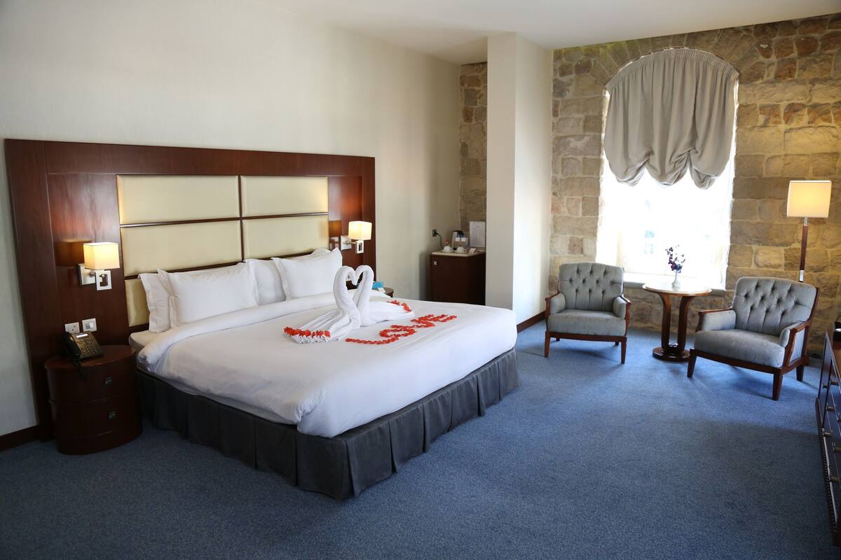 Une chambre d’hôtel avec un grand lit, deux tables de chevet, une commode, une chaise, une petite table et une lampe.