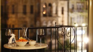 A table with a bowl of food and two wine glasses, set against a balcony railing with a blurred building in the background. - Grand Kadri Hotel (Zahlé)