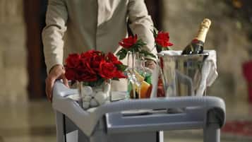 Un chariot portant une bouteille de champagne, un vase rempli de roses rouges et un verre de jus d’orange.