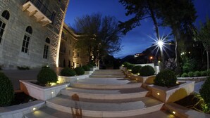 A stone building with a grand staircase leading to a balcony, surrounded by well-lit landscaping and trees. - Grand Kadri Hotel (Zahlé)