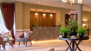 A hotel lobby with a reception desk, seating area, and decorative plants.