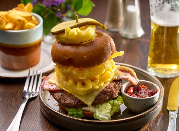 A burger with bacon, lettuce, and a pickle on top, served with fries and ketchup. - Tulfarris Hotel & Golf Resort (Blessington)