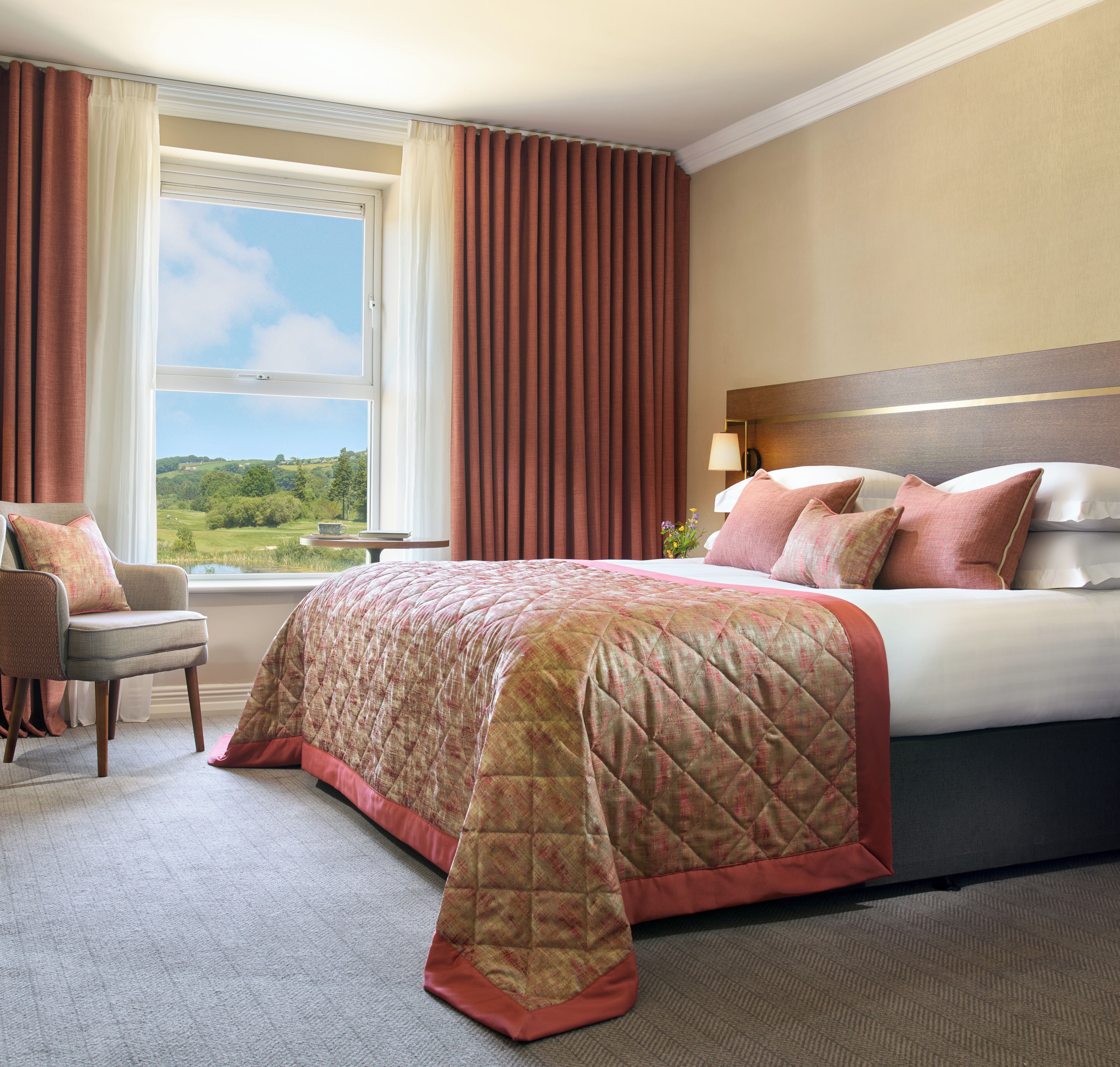 Habitación de hotel con una cama grande, una silla, una mesita y vistas al exterior.