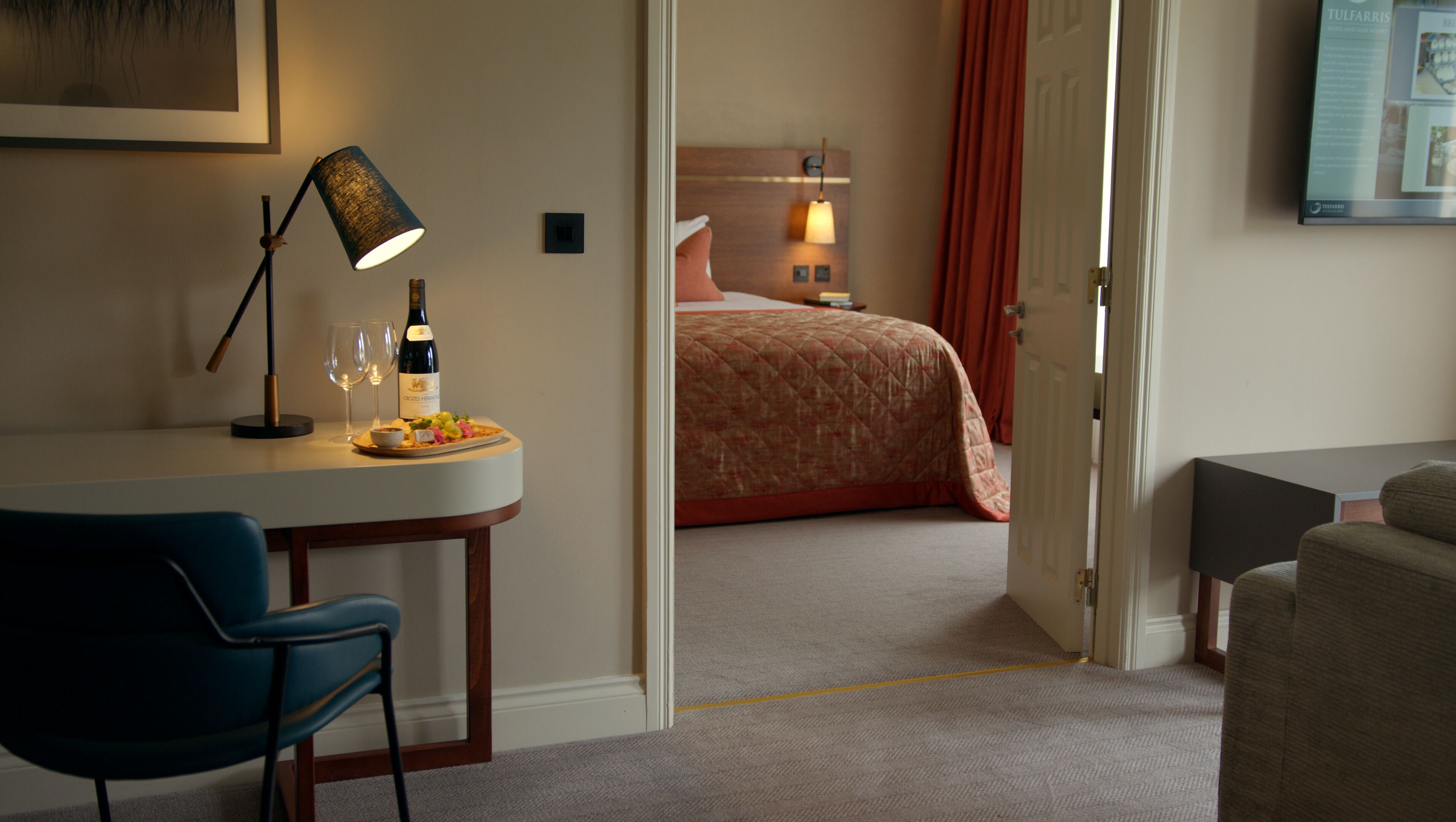 Una habitación de hotel con escritorio, silla, cama y una puerta que da a otra habitación.