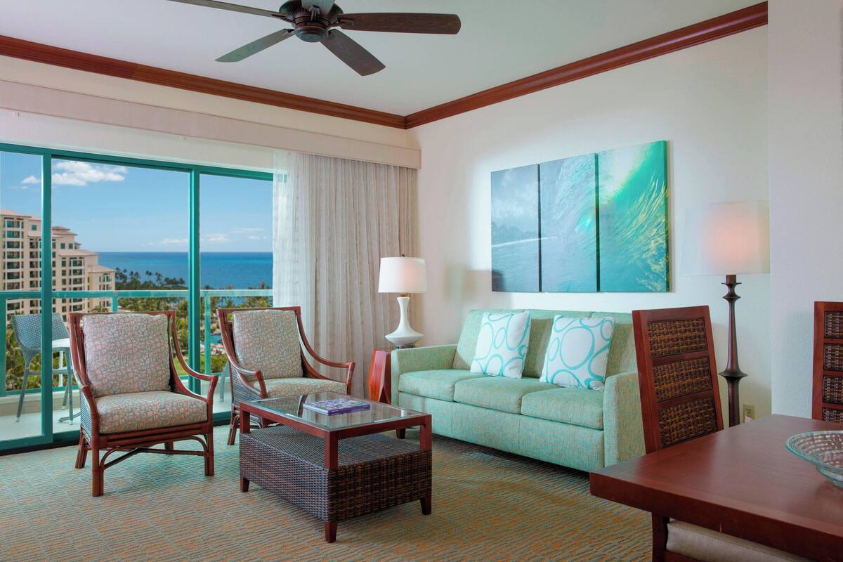 A hotel room with a balcony, a sofa, two armchairs, a coffee table, and a dining table.