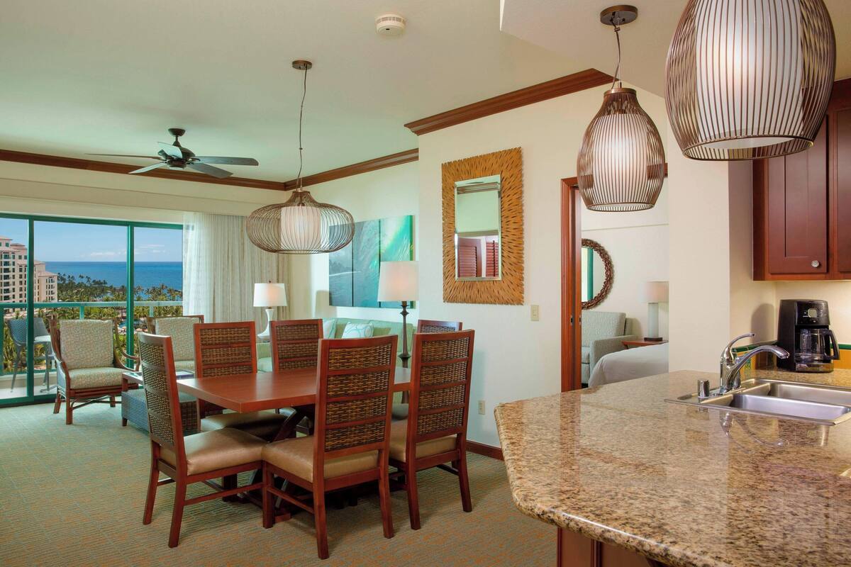 A hotel room with a dining area, a kitchen with a granite countertop, and a view of the ocean.