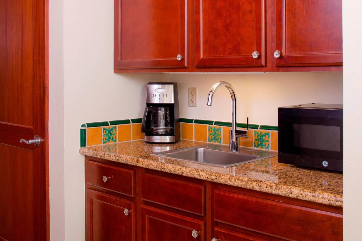 A kitchen with wooden cabinets, a granite countertop, a coffee maker, a sink, and a microwave.
