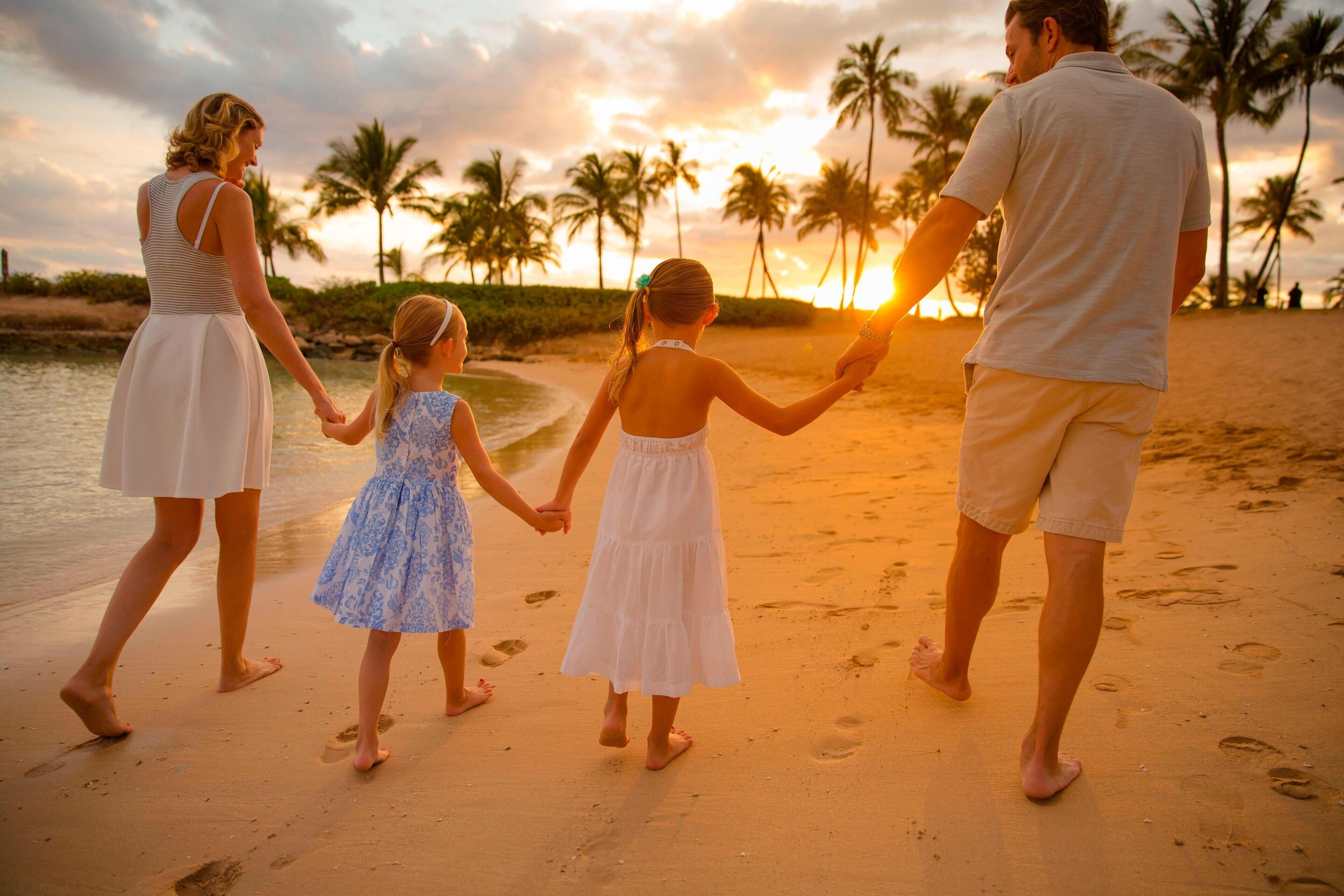 Una familia caminando por la playa, con palmeras y el sol poniéndose al fondo.