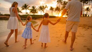 Una familia caminando por la playa, con palmeras y el sol poniéndose al fondo.
