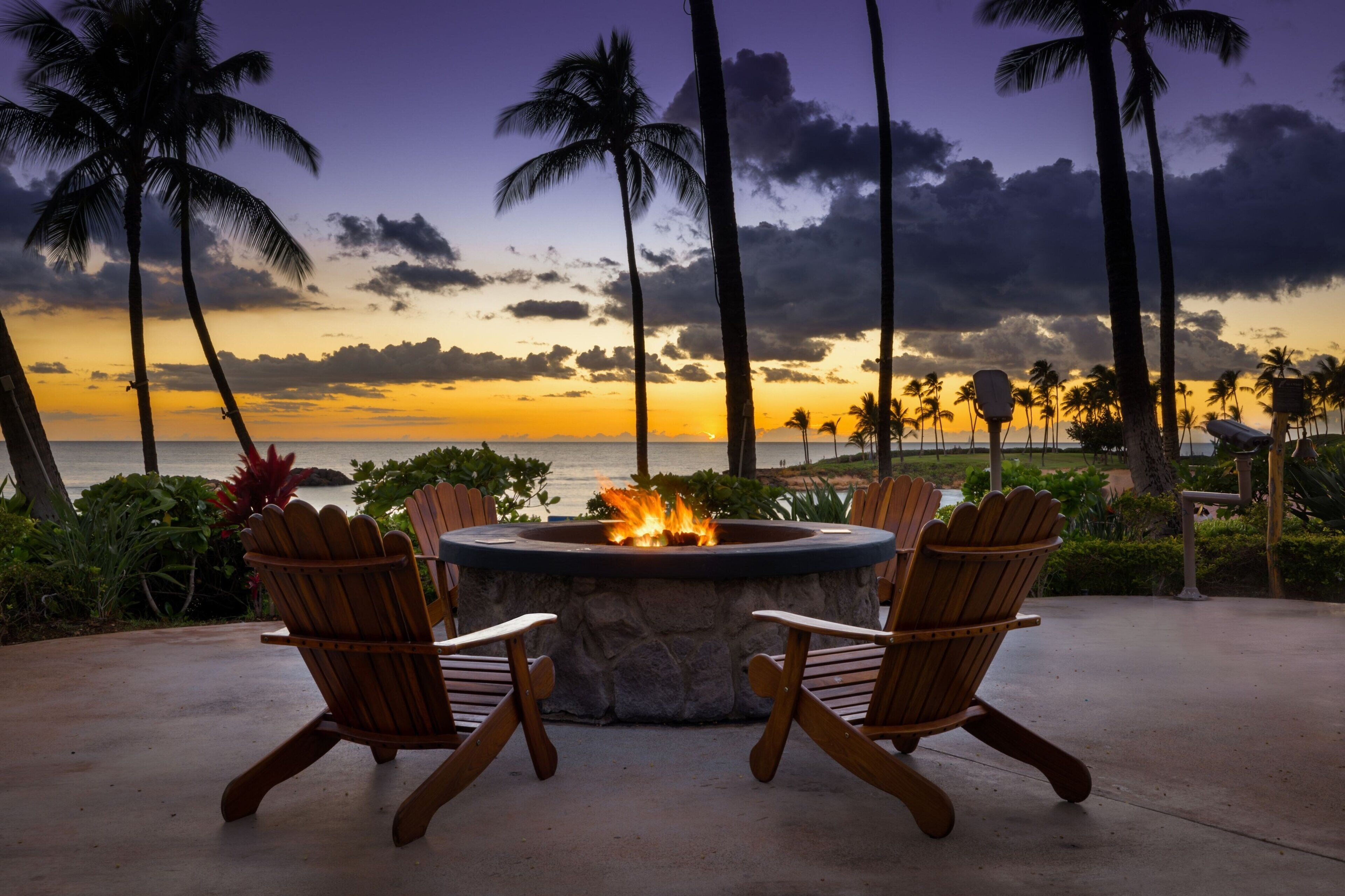 Un hogar con asientos en un entorno tropical, con vistas a la puesta de sol y al océano.