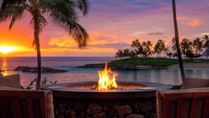 A fire pit with a view of the ocean and palm trees at sunset.