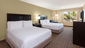 A hotel room with two beds, a desk, a chair, and a large window with a view of palm trees.