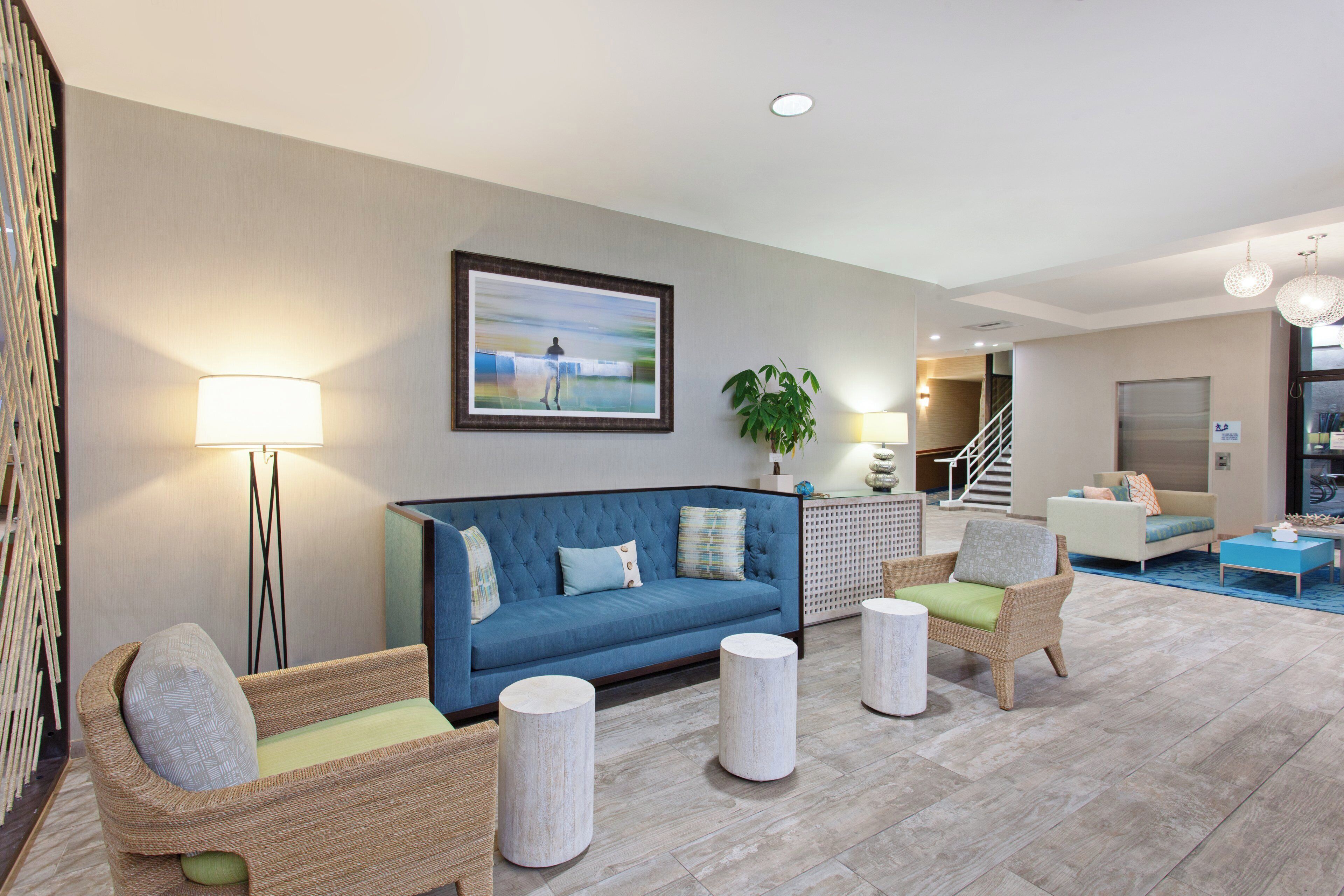 A modern living room with a blue sofa, wicker chairs, and a painting on the wall.