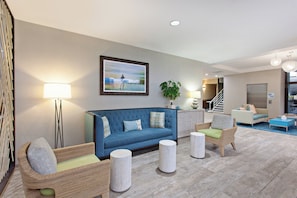A modern living room with a blue sofa, wicker chairs, and a painting on the wall.