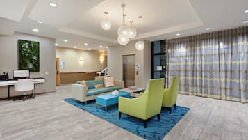 A hotel lobby with a reception desk, a sofa, chairs, a coffee table, and a decorative wall.