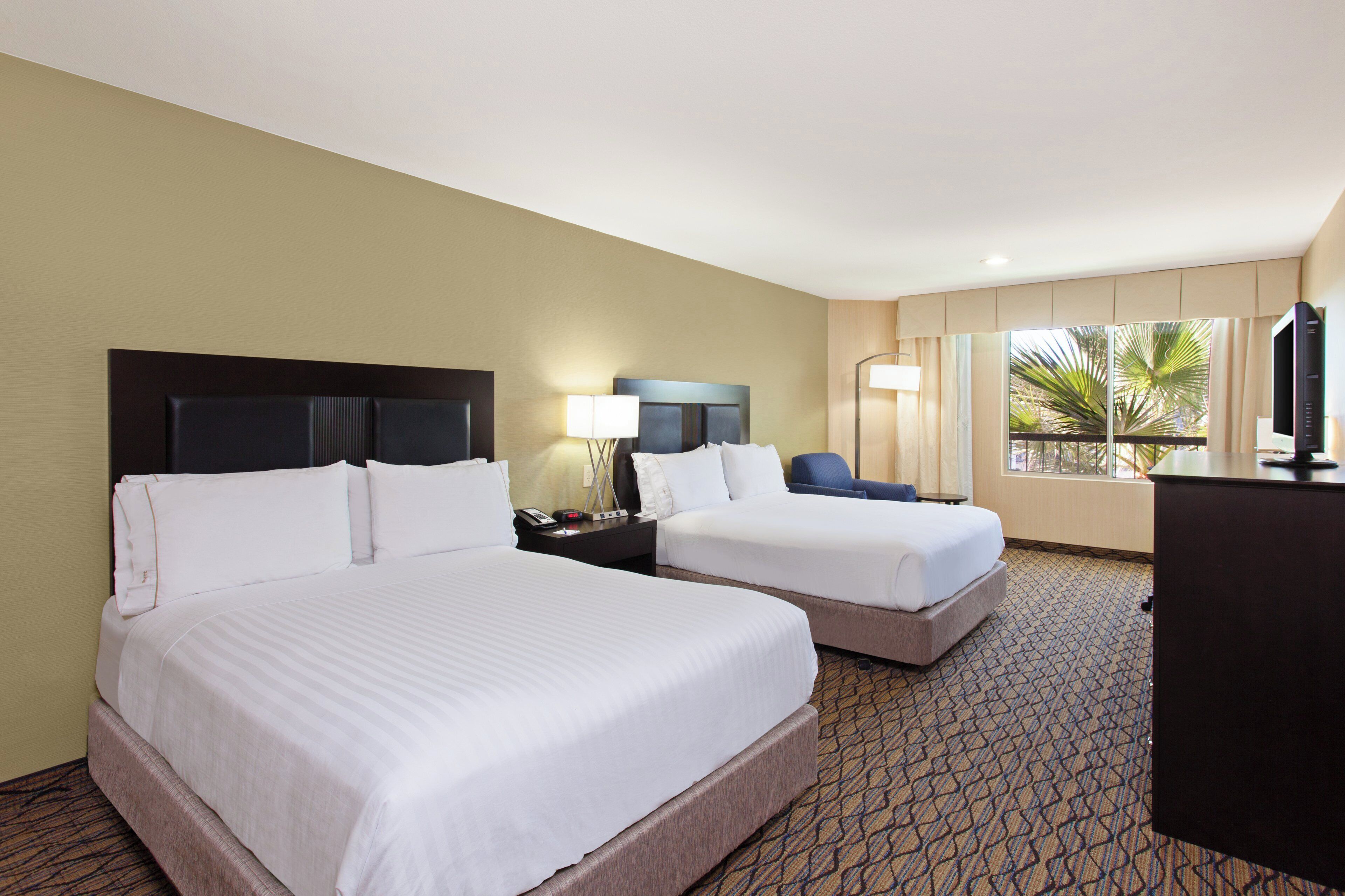 A hotel room with two beds, a desk, a chair, and a television.