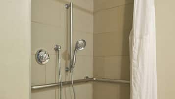 A shower area with a white shower curtain, a handheld showerhead, and a wall-mounted faucet.